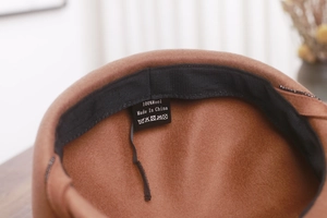 Detail view of the brown wool newsboy hat featuring 100% wool label and inner black sweatband