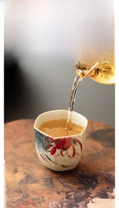 Action shot of tea pouring into a handcrafted ceramic cup with red fish and floral patterns