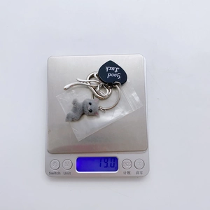 Gray flocked cat keychain with Good Luck heart charm being weighed on a scale