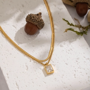 Gros plan d'un collier doré double épaisseur avec zircon carré sur une base en pierre