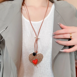 Detailed view of large gold hollow heart pendant with red charm on brown cord