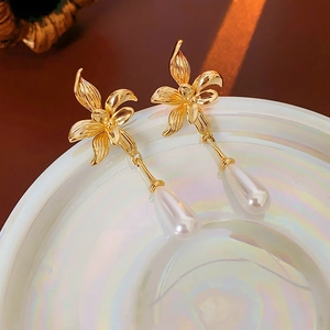 Macro shot of 14K gold plated flower earrings with drop pearls on white porcelain