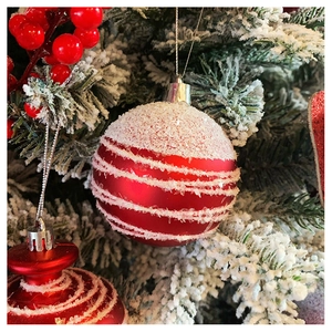 Close-up of red Christmas baubles and bell ornaments with white snow stripes on pine branches