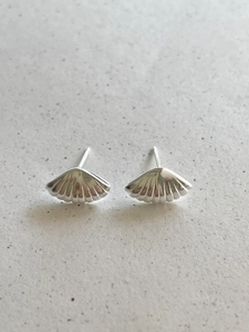 Macro detail of silver shell stud earrings with textured surface on a grey stone background