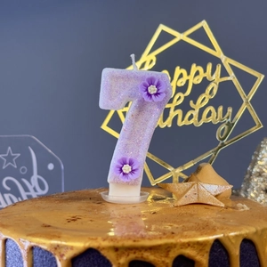 Detail of purple number 7 birthday candle with glitter and 3D flower on a cake