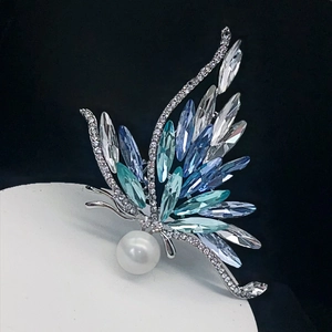 Broche papillon argentée élégante avec cristaux bleus et une grande perle sur fond blanc