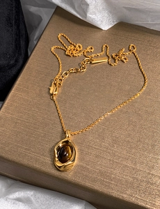 Macro detail of gold-plated tiger eye stone oval pendant necklace on textured gold box