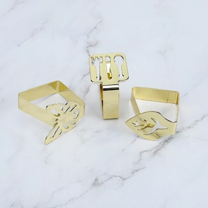 Three golden leaf, butterfly, and cutlery table cloth clips on white marble surface