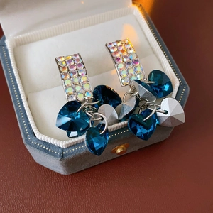 Macro detail of long tassel earrings with blue heart crystals on a velvet jewelry box