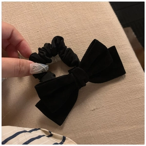 Close-up of a vintage black velvet bow hair scrunchie held by hand against beige cloth