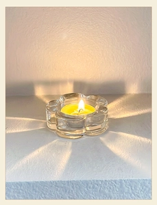 Detail view of flower-shaped glass candle holder with warm lit tea light and soft shadow