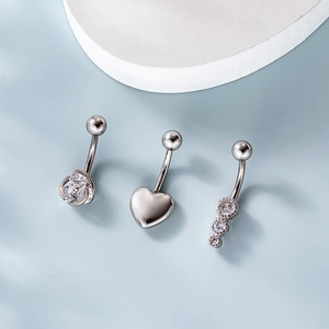 Three surgical steel belly rings featuring cubic zirconia round and heart designs on blue background