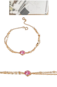 Detail of pink oval gemstone on gold-plated double-chain bracelet with elegant beads