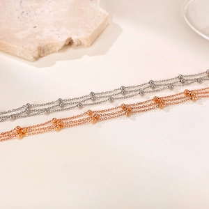 Layered stainless steel anklets in silver and rose gold with delicate metal beads