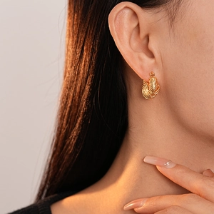 Detail of gold woven U-shaped earrings on model highlighting the warm metallic texture