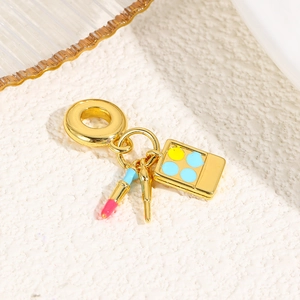 Macro detail of gold makeup charm with lipstick, brush, and palette on white surface