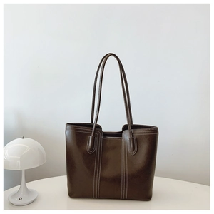 Detail of dark brown leather tote bag with white contrast stitching on a minimalist stand