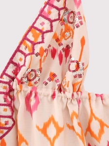 Détails de paillettes et broderies sur un haut en lin beige avec des motifs floraux oranges