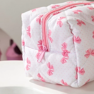 Gros plan d'une trousse à maquillage blanche matelassée avec motifs de nœuds roses et coutures