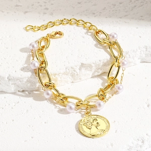 Close-up of gold chain bracelet featuring lilac pearls and Elizabeth II coin pendant