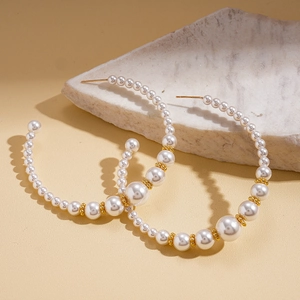 Detail of C-shaped pearl hoop earrings with gold beads on elegant marble surface