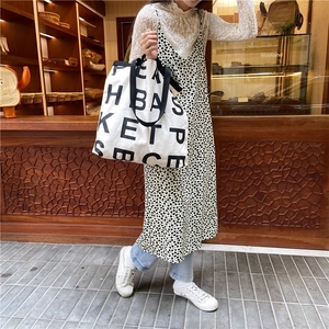 Large beige canvas tote bag with black letter print shown in a street lifestyle setting