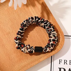 Detailed view of leopard print hair scrunchie with black buckle on a wooden tray