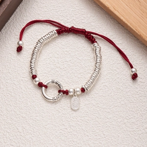 Detail of red braided lucky bracelet with silver pendant and auspicious engraving