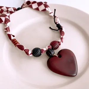 Retro beaded fabric heart pendant necklace with checkered cord on a white plate