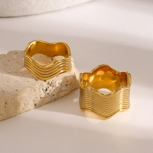 Macro view of two wavy multi-layer gold plated rings on a neutral stone background