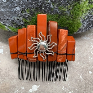Detail of reddish stones and silver sun charm hand-wrapped on a metal hair comb