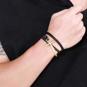 Close-up of a golden Ankh cross charm on a black braided leather multi-layer bracelet