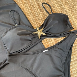 Détail d'un bikini noir avec boucle étoile de mer dorée et jupe en tulle sur un tapis