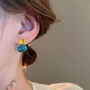 Close-up of model wearing transparent yellow and blue double-sphere glass earrings