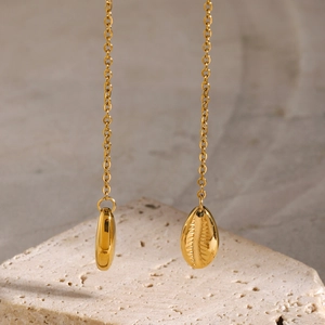 Detail of 18k gold plated long chain shell pendant earrings on a textured stone background