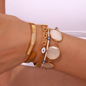 Detail of layered gold-plated chain bracelet with evil eye charm and baguette zircon stones