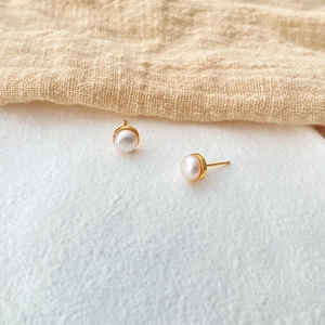 Close-up of elegant small white pearl stud earrings on 18K gold plated brass base