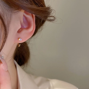 Close-up of elegant gold J-hook earring featuring a single sparkling zircon on a model