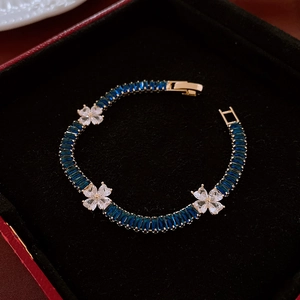 Detailed shot of gold bracelet with deep blue gemstone and white zircon clover flowers