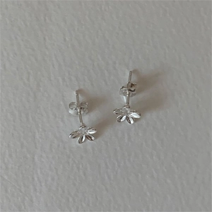 Detail view of small silver floral stud earrings with six petals on grey surface