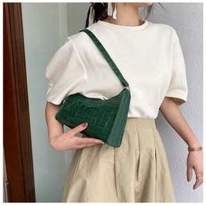 Close-up of a dark green crocodile pattern underarm bag worn by a model in natural light