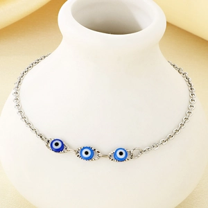 Detail shot of a silver chain featuring three blue evil eye charms draped on a white vase