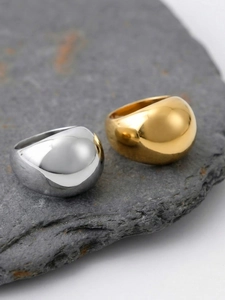 Close-up of polished gold and silver chunky round rings on a grey stone background