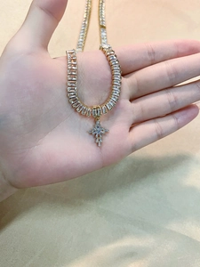 Detailed view of a gold cross pendant necklace with sparkling rectangular crystal stones