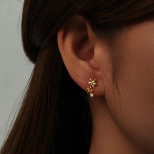 Close-up of a 925 silver gold-plated star and flower earring with zircon on an ear