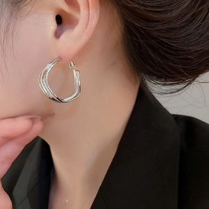Close-up of irregular silver-tone hoop earrings with glitter texture on a model's ear