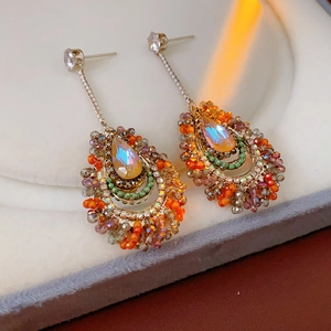 Macro shot of silver needle tassel earrings with orange teardrop crystals and gold chains