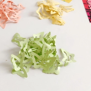 Flat lay view of pastel green, pink, and yellow butterfly hair clips on a white background