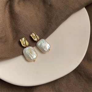Macro detail of French vintage baroque pearl earrings with textured gold square pendants