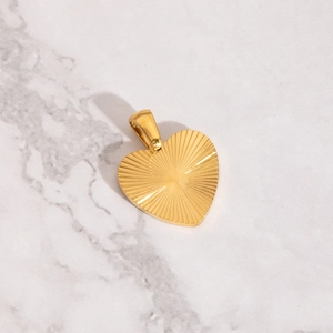 Macro detail of a golden heart pendant with radial texture on white marble background